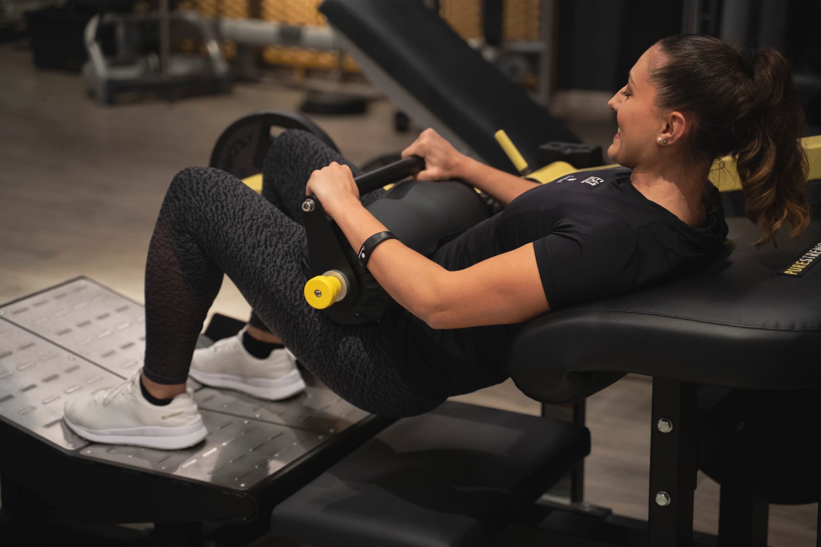 Una cliente sorride durante un hip thrust seguita dal suo trainer