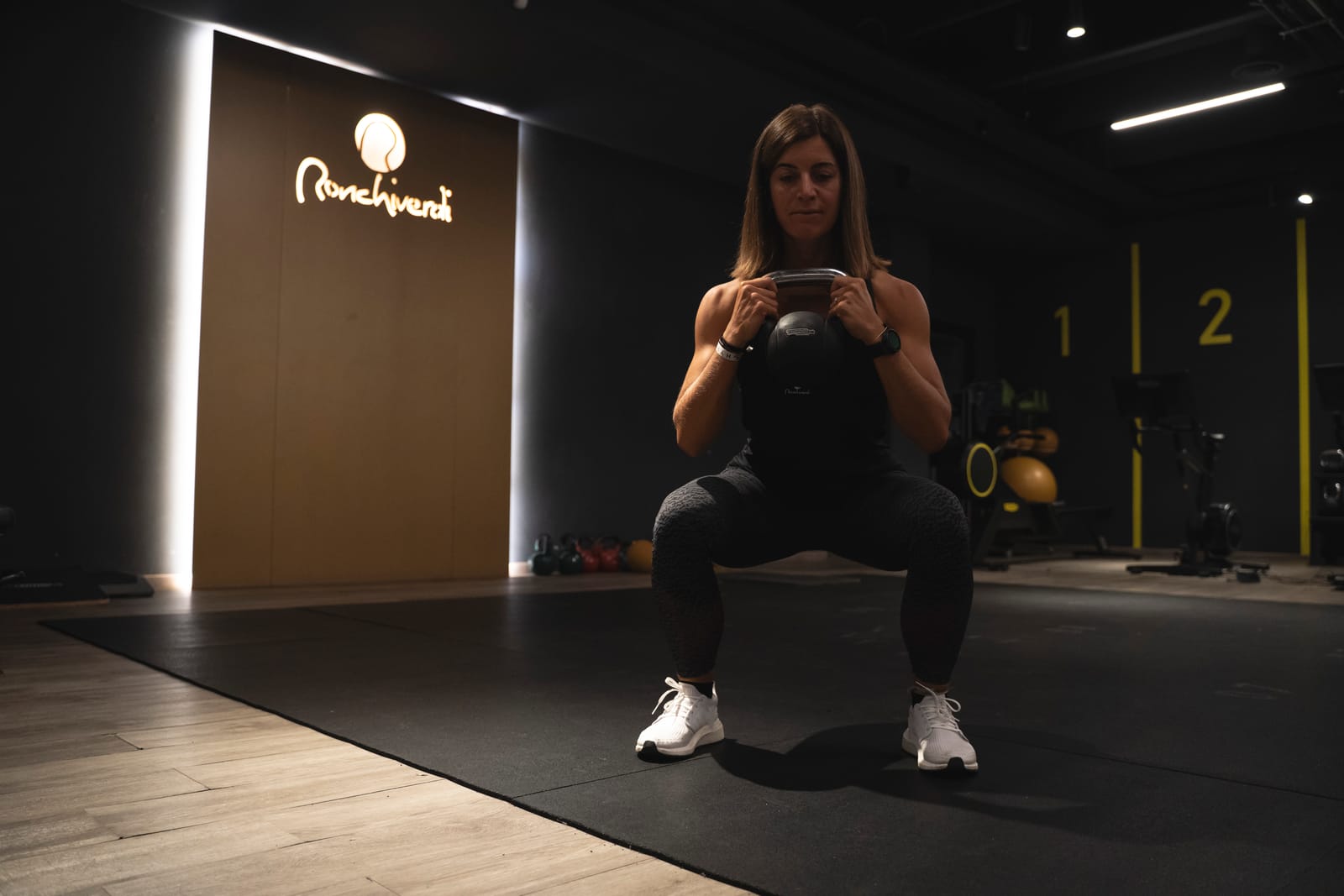 Squat con kettlebell nella Skill Area, davanti alla parete con il logo Ronchiverdi